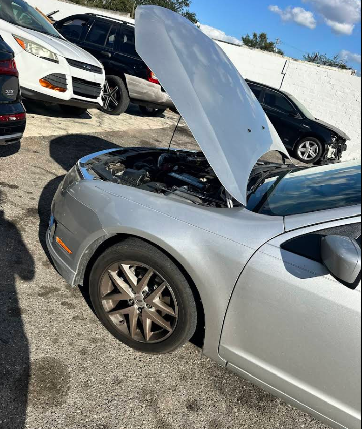Silver coupe with hood up in the shop's back lot